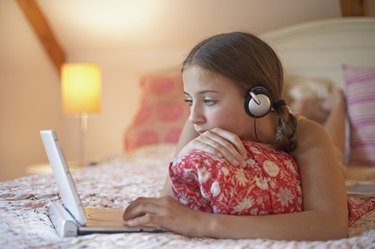 Teenage girl lying on a bed using a laptop
