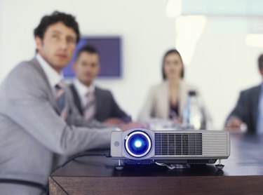Businessmen and women watching film, projector on table