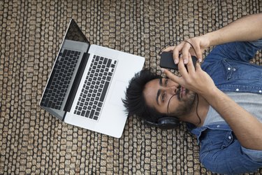 Asian man lying on the floor with laptop and phone.