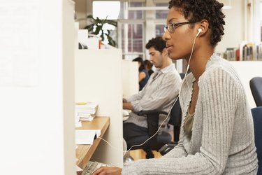 Female office worker at desk, wearing earphones