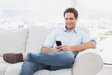 Cheerful man sitting on the couch using his smartphone
