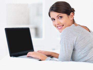 Young woman smiling in bed with a laptop
