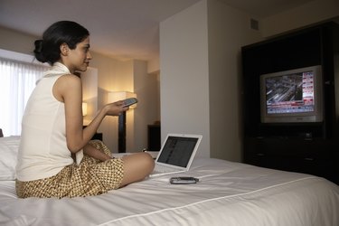 Businesswoman on hotel bed watching financial news