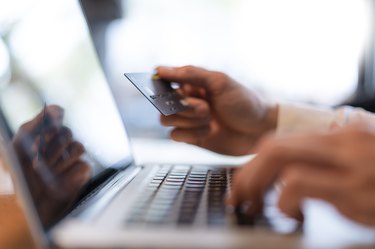 Man's hands holding credit card and typing on computer, close-up