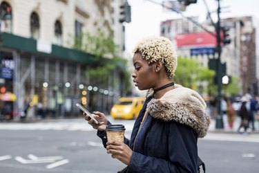 USA, New York City, fashionable young woman with coffee to go looking at cell phone on the street